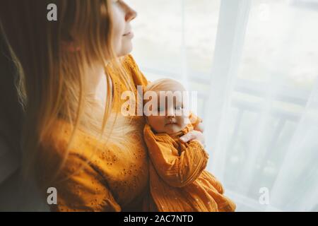 Fille mère avec bébé bébé vie familial maman et enfant ensemble à la maison de vacances fête des Mères la maternité concept robe couleur moutarde Banque D'Images