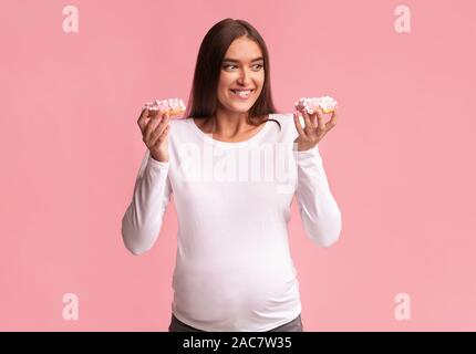 Fille enceinte Holding Donuts debout sur fond rose, Studio Shot Banque D'Images