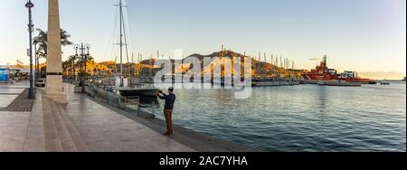 Cartagena, Espagne - décembre 2, 2017 : Yung homme fait photo de promenade en utilisant votre smartphone. Vue panoramique du port de plaisance de Murcia Cartagena heure du coucher de soleil. Banque D'Images