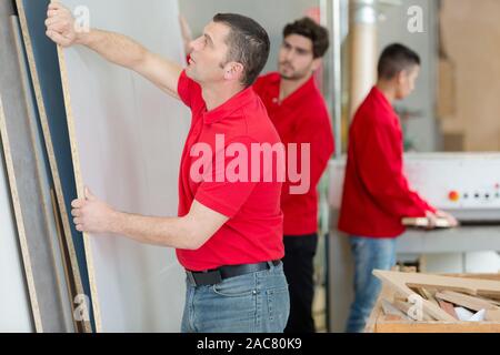 Les charpentiers du déplacement d'une grande feuille de contreplaqué dans l'atelier Banque D'Images