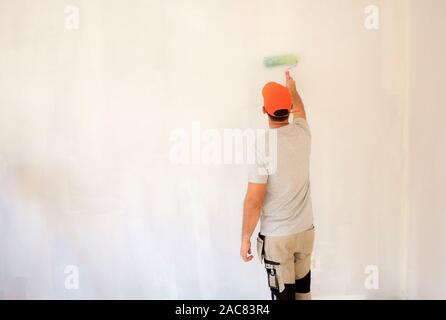 Vue arrière coup de jeune homme à l'aide de rouleau à peindre en peignant le mur. Banque D'Images