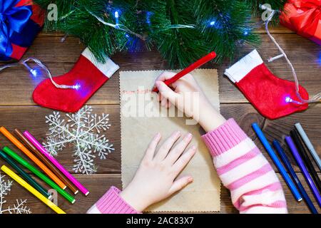 Les enfants lettre au Père Noël. Petite fille écrit une lettre avec des feutres de couleur sur une table en bois avec des décorations de Noël sur l'ancien Banque D'Images