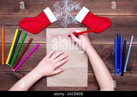 Les enfants lettre au Père Noël. Petite fille écrit une lettre avec des feutres de couleur sur une table en bois avec des décorations de Noël sur l'ancien Banque D'Images