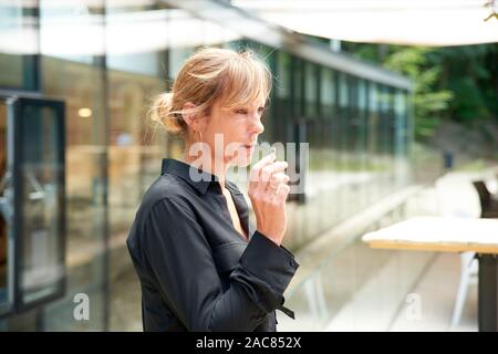 Portrait de femme d'âge moyen cigarette tout en se tenant à l'extérieur. Banque D'Images