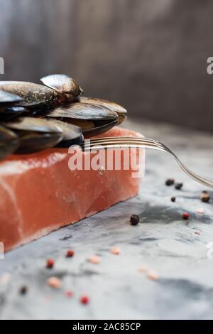 Bloc de sel de cuisine. Les coquilles des moules crues dans le rôti de l'himalaya sels rose sur fond de béton vue latérale copy space Banque D'Images