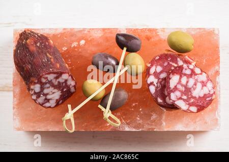 Salami fumé, vert et olives calamata servi sur bloc de sel rose hymalayan vue aérienne Banque D'Images