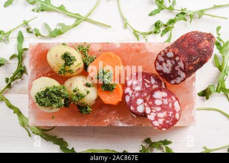 Salami fumé, pommes de terre, les carottes et la roquette avec sauce Chimichurri vert servi comme apéritif sur hymalayan de bloc de sel rose Vue de dessus Banque D'Images