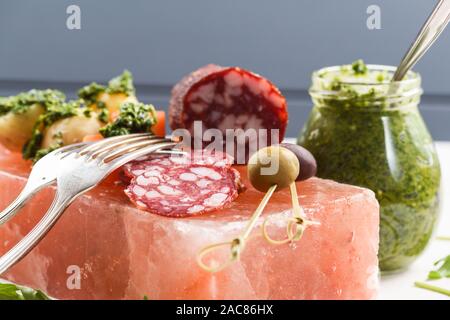 Amuse-gueule servis sur hymalayan de bloc de sel rose : salami fumé, pommes de terre et les olives avec sauce Chimichurri vert closeup Banque D'Images