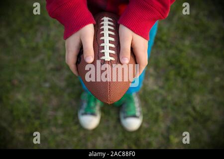 Vue de dessus sur les mains du gamin boy holding football sur le stade lors d'une journée ensoleillée. Enfant prêt à jeter un ballon de football. Sport concept. Activités sport f Banque D'Images