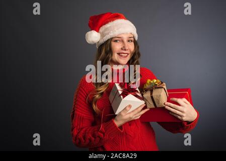 Surpris fille avec un tas de cadeaux dans les mains. Une belle fille avec un visage exprimant l'émotion de wow, dans un chandail rouge et un chapeau de Noël Sa Banque D'Images