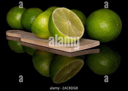 Groupe de quatre ensemble deux moitiés de sour lime vert sur planche à découper en bois isolé sur verre noir Banque D'Images