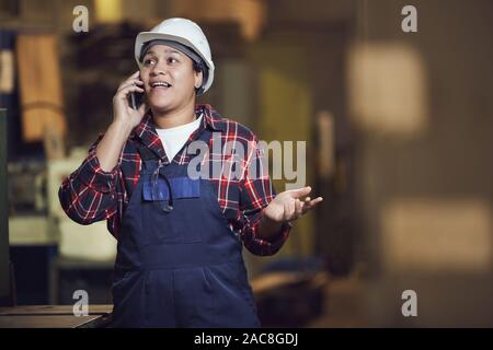 Taille portrait de femme moderne s'exprimant par téléphone et gesticulant debout par des unités utilisées dans l'industrie, copy space Banque D'Images