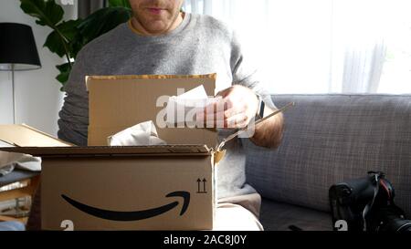 Paris, France - Oct 7, 2019 : Vue de face de l'homme curieux unboxing déballage sur salon canapé les derniers colis reçu d'Amazon Premier lire la facture et inclus papier Remarque Banque D'Images