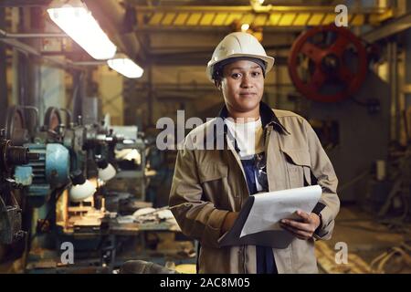 Taille portrait of female worker holding clipboard tout en supervisant la production à l'usine, copy space Banque D'Images
