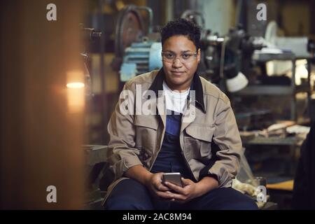 Portrait de race mixte contemporain woman smiling at camera tout en se posant dans l'atelier d'usine Banque D'Images