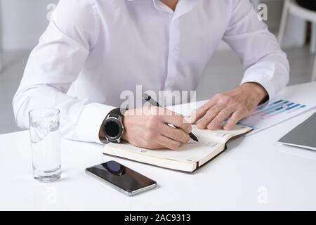 Mains d'entrepreneur mâle en chemise blanche décisions notes de travail ou d'un plan pour la journée en position assise par 24 Banque D'Images