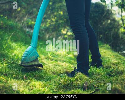 Une jeune femme est la coupe à l'aide d'un strimmer herbe pelouse Banque D'Images
