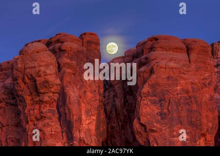 Une presque pleine lune se lève au-dessus de formations rocheuses dans le jardin d'Éden dans Parc National Arches dans Moab, Utah. Banque D'Images