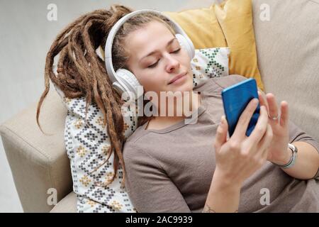 Jolie jeune femme avec des dreadlocks reposant à écouter de la musique dans le casque Banque D'Images