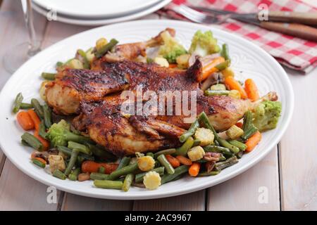 En vertu d'un poulet, de brique ou de pollo al mattone, avec des légumes grillés sur un grand plat blanc Banque D'Images