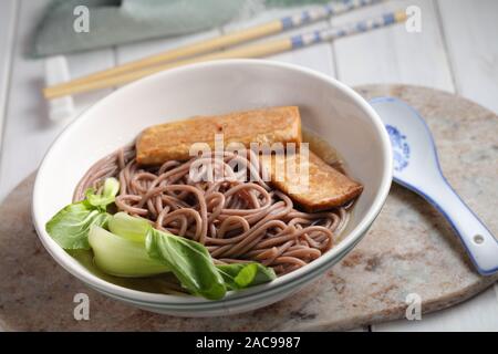 Partie de la soupe aux nouilles soba avec des tranches de tofu frit et feuilles de bok choy Banque D'Images