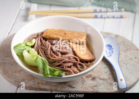 Partie de la soupe aux nouilles soba avec des tranches de tofu frit et feuilles de bok choy Banque D'Images