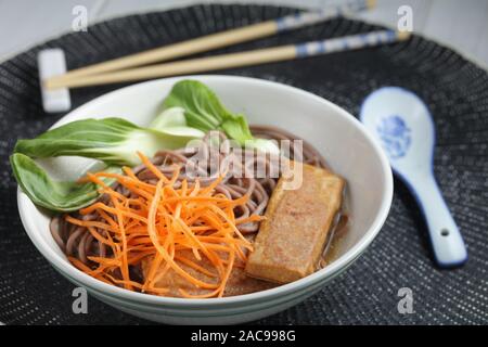 Partie de la soupe aux nouilles soba avec des tranches de tofu frit, carotte, feuilles de bok choy et Banque D'Images