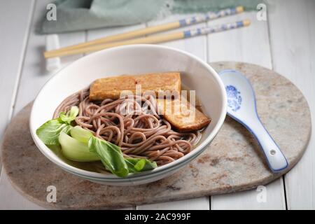 Partie de la soupe aux nouilles soba avec des tranches de tofu frit et feuilles de bok choy Banque D'Images