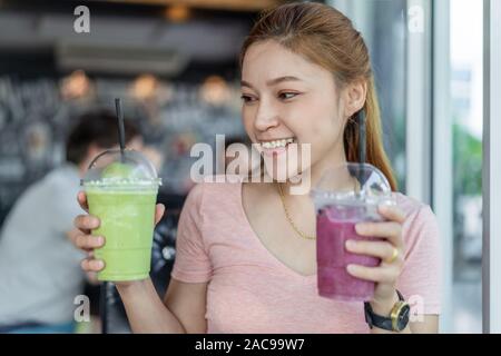 Femme tenant un verre de thé vert frappe et de bleuet smoothies en cafe Banque D'Images