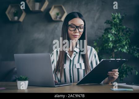 Photo de Happy cute joli dame d'affaires ayant atteint beaucoup d'objectifs à son jeune âge en spectacles holding clipboard avec contrat important dans Banque D'Images