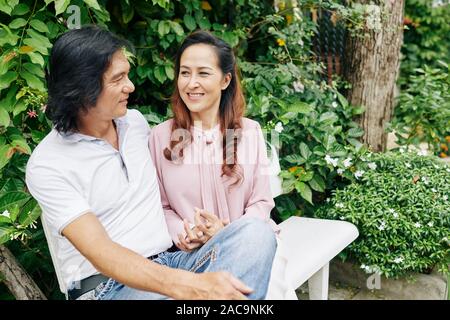 Smiling mature couple amoureux assis sur un banc, discuter et profiter de date romantique Banque D'Images