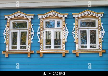 Plyos, la Russie, le 1 décembre 2019 : Blue façade d'une maison en bois. Trois fenêtres avec du blanc et jaune sculpture sur bois décoratif cadre. Style folklorique russe. Vue avant close up image stock. Banque D'Images