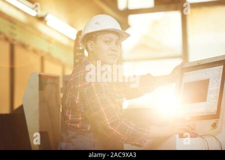 Portrait aux teintes chaleureuses de femme afro-américaine à la caméra à tout en travaillant à l'usine de production à la lumière du soleil, copy space Banque D'Images