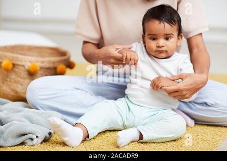 African Baby Boy assis sur le plancher avec la mère assis derrière lui et tenant sa main passer du temps à la maison Banque D'Images
