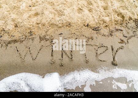 Vague d'écume lave le mot hivernent au large de la plage de sable, l'hiver s'en va avec l'arrivée de l'été Banque D'Images