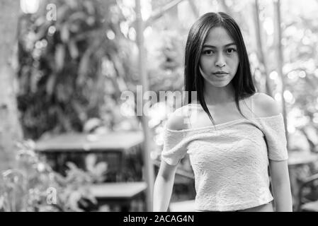 Belle asiatique jeune adolescente à se détendre jardin verdoyant entouré de plantes saines et arbre Banque D'Images