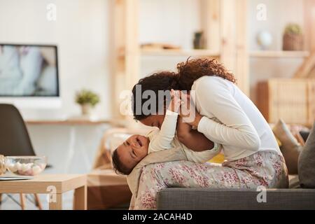 Vue de côté d'Entraide Solidarité portrait Mère embrassant mignon bébé garçon tout en jouant à la maison, copy space Banque D'Images