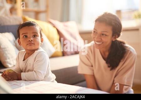 Smiling young mother sitting et jouant avec son petit enfant sur le canapé dans la chambre Banque D'Images