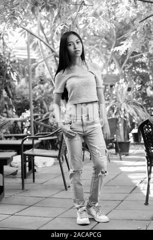 Full body shot of young beautiful Asian teenage Girl standing tout en se posant au café-restaurant en plein air entouré par la nature Banque D'Images