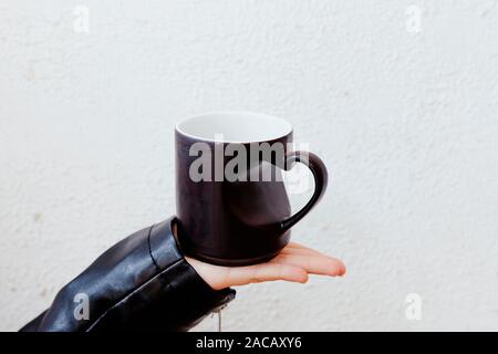 Méconnaissable femme tenant une tasse avec une poignée en forme de coeur. Tasse de café ou de couleur noire avec la main en forme de coeur. Banque D'Images
