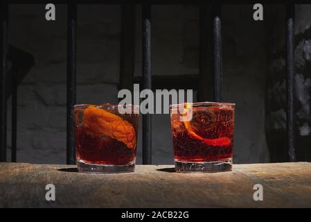 Deux verres à whisky fissurée. Cocktails d'alcool rouge sur la table en bois. Servi avec de la glace et la peau d'orange. Negroni ou Boulevardier. Banque D'Images