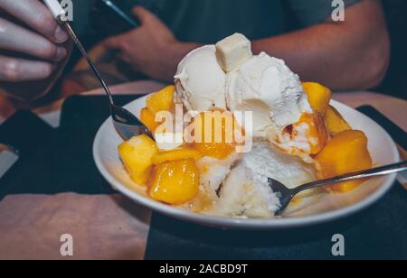 Vue rapprochée de l'homme est de manger froid et de mangue fraîche Bingsoo - coréen shaved ice avec morceaux de mangue et boule de glace Banque D'Images