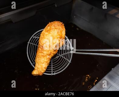 Des poissons cuits et fourrés sortant d'une friteuse dans une boutique de poissons et de chips au Royaume-Uni Banque D'Images