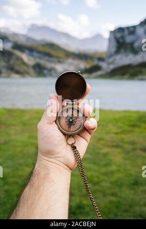 Une main tient une boussole dans un paysage de montagne et lac Banque D'Images