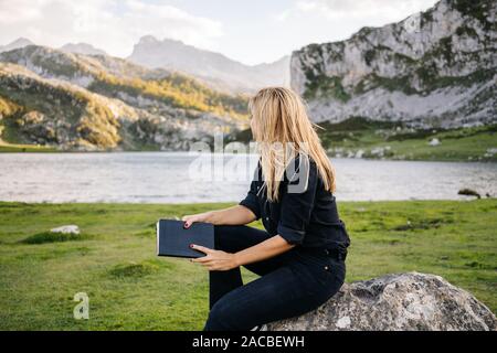 Un beau portrait femme blonde lit un livre dans un paysage montagneux avec un lac Banque D'Images