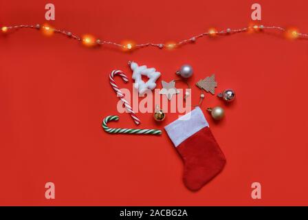 Composition de Noël. Chaussette de Noël avec des boules de Noël, des jouets, sucettes et garland sur fond rouge. L'hiver, Noël, Nouvel an concept. Banque D'Images