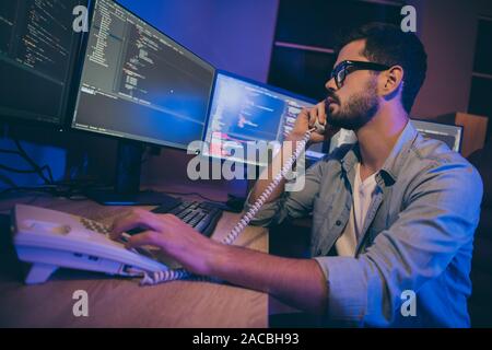 Photo du profil de l'informaticien guy travailler tard dans la nuit assis chaise confortable bureau moniteurs parlant à la site web de téléphone correct expert débogage Banque D'Images