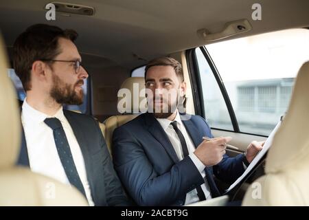 Jeune homme barbu tenant le document et en parler à son partenaire pendant la conduite dans la voiture Banque D'Images
