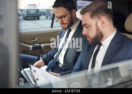 Deux jeunes hommes assis sur siège arrière et working on laptop ensemble lors de la conduite sur un taxi Banque D'Images