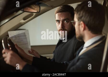 Jeune homme barbu tenant contrat et parler à d'autres l'homme au sujet de l'achat de la voiture Banque D'Images